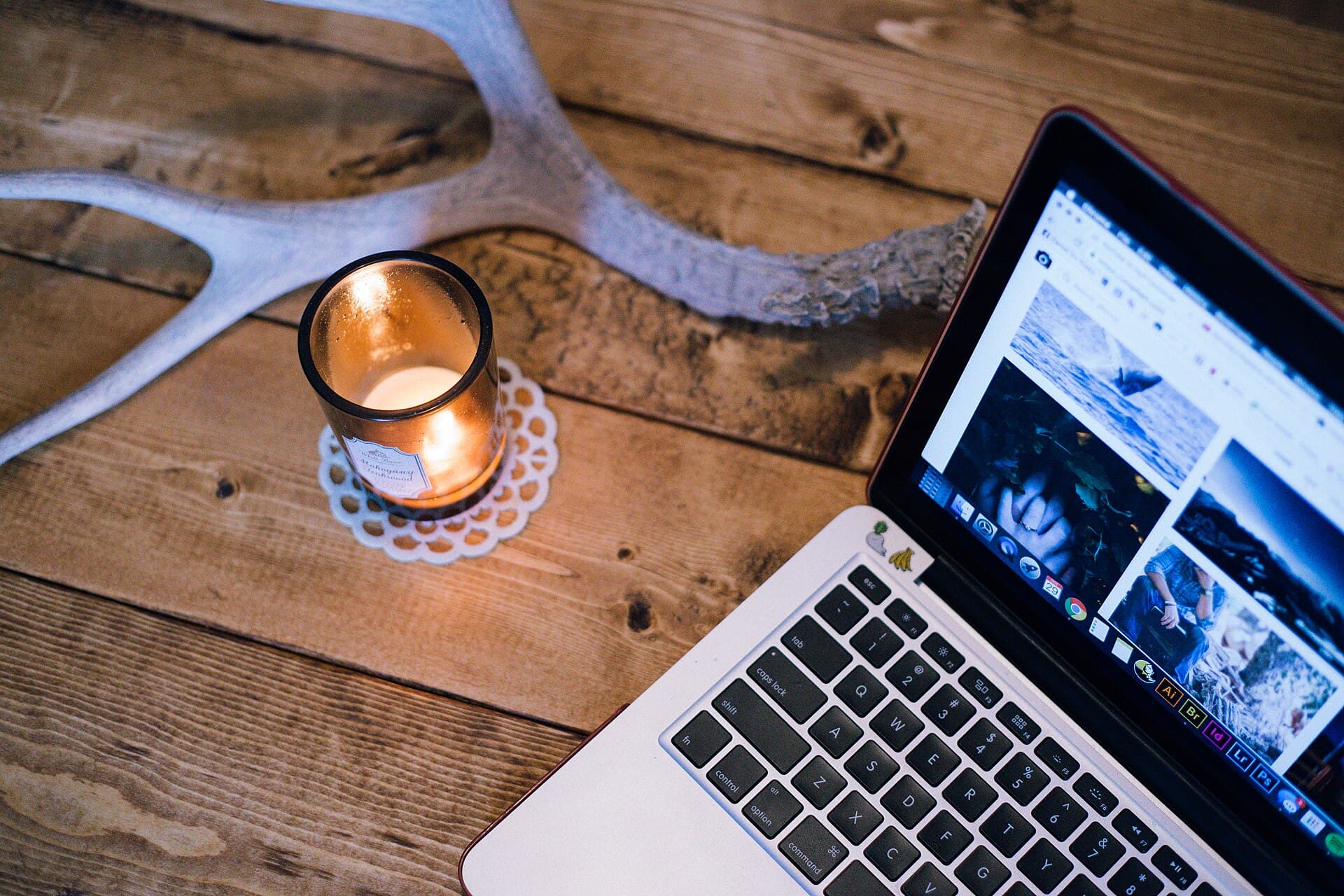 A laptop beside a lit candle and an antler on a wooden table